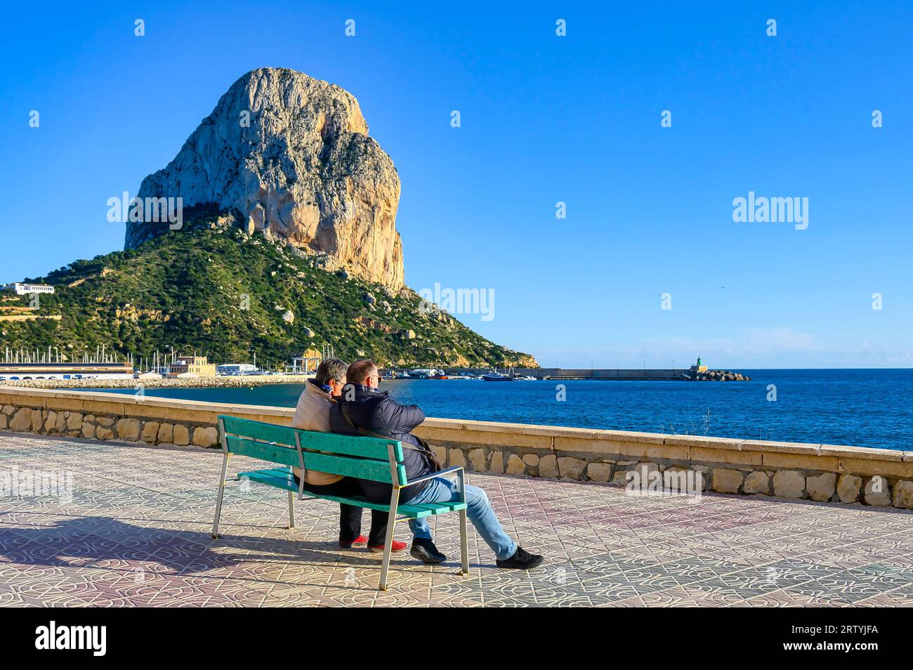 Calpe, Spanien - 10. Januar 2023: Ein Paar sitzt auf einer Bank und blickt auf den Strand Stockfoto