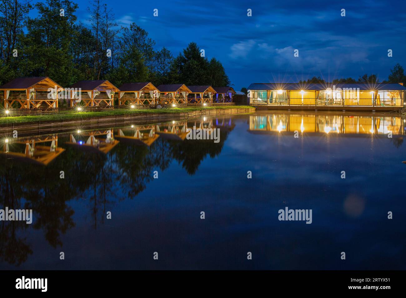 Reihe von hölzernen Pavillons zum Entspannen am See und glühender Pavillon oder Restaurant am Abend Stockfoto