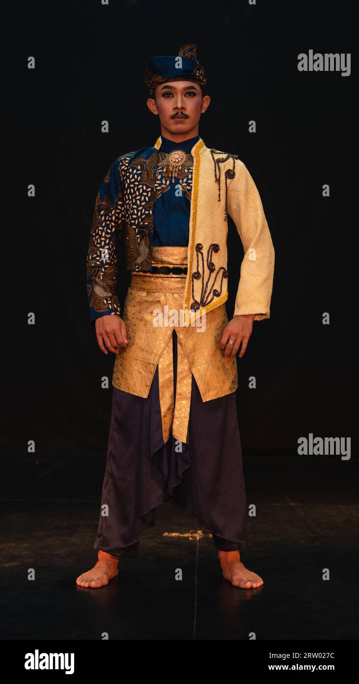 Ein asiatischer Mann, der ein traditionelles Kostüm mit schönen Motiven auf seinem Hemd trägt und ein Bandana trägt, das Bendo genannt wird, in einem Raum mit schwarzem Hintergrund Stockfoto