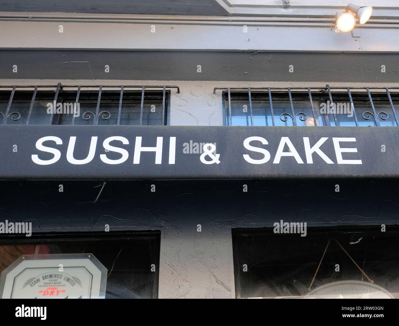 Allgemeines Sushi und Sake in weißen Großbuchstaben auf verwitterter und getragener schwarzer Leinwand über einem japanischen Restauranteingang; asiatische Speisen und Getränke. Stockfoto