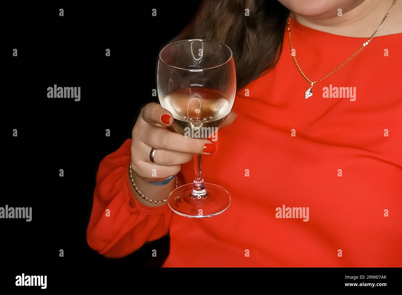 Eine Frau in roter Kleidung hält ein Glas weißen Alkohol, Champagner, auf schwarzem Hintergrund, Wochenendatmosphäre. Stockfoto