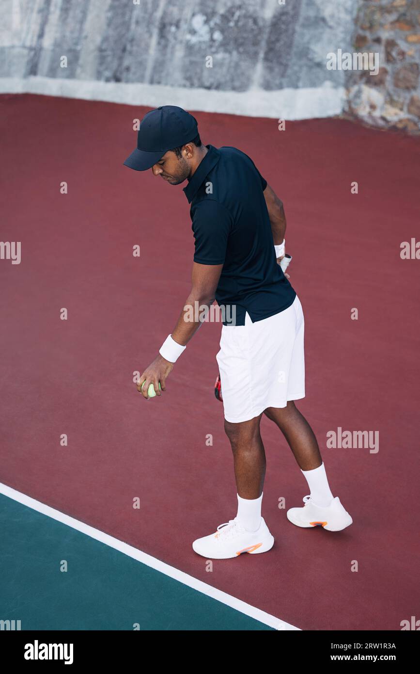 Junger Mann, der den Ball in der Baseline auf dem Hartplatz für den Serve hüpft Stockfoto