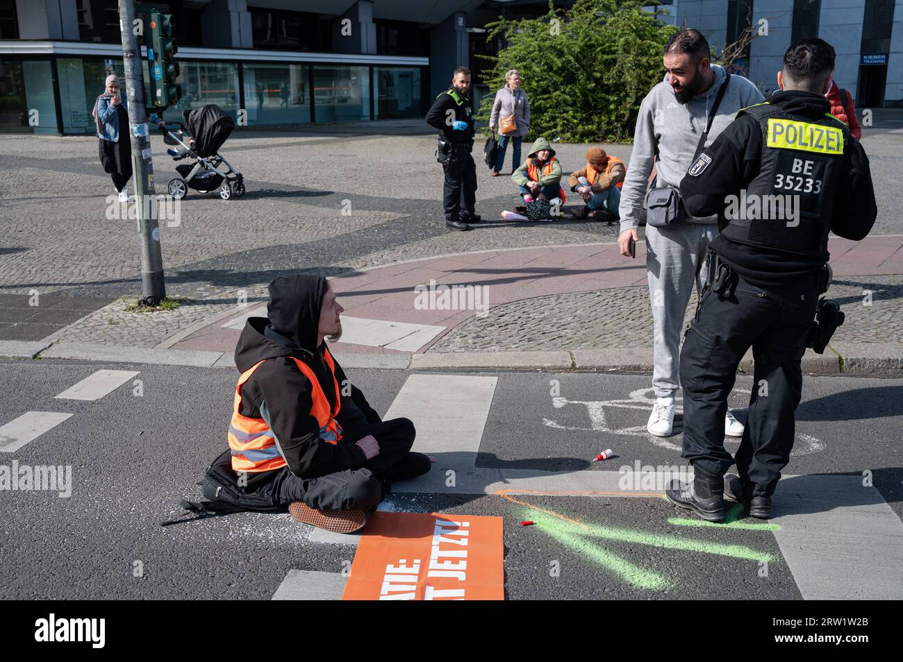 28.04.2023, Deutschland, Berlin, Berlin - Europa - Ein Klimademonstrator der letzten Generation hält zusammen mit anderen Teilnehmern an der Fahrbahn eines m fest Stockfoto