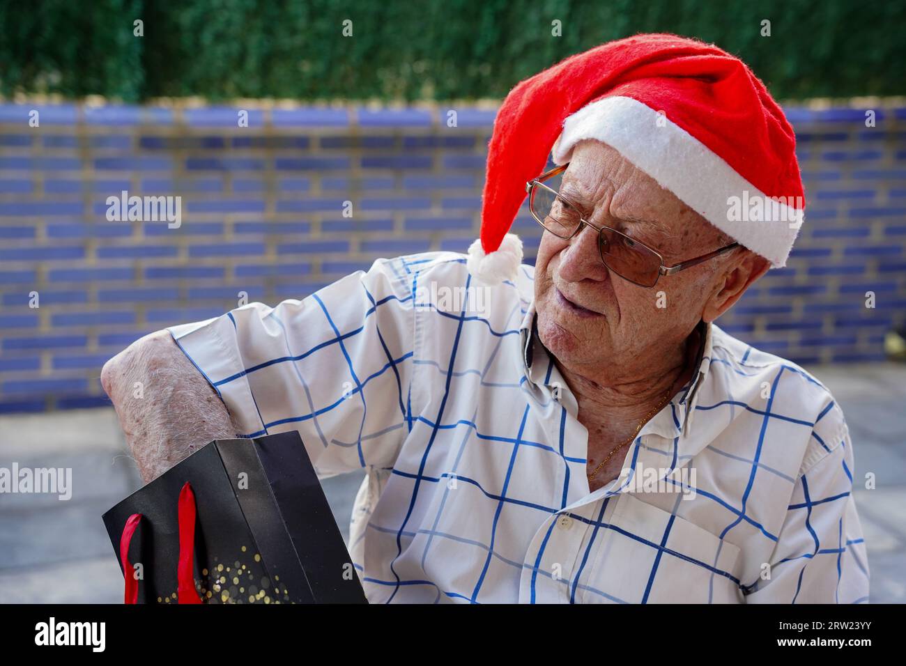Pensionierter Mann mit weihnachtsmannhut und weihnachtsgeschenk im Sommer. Altersleben im Xmas. Frohe weihnachten Stockfoto