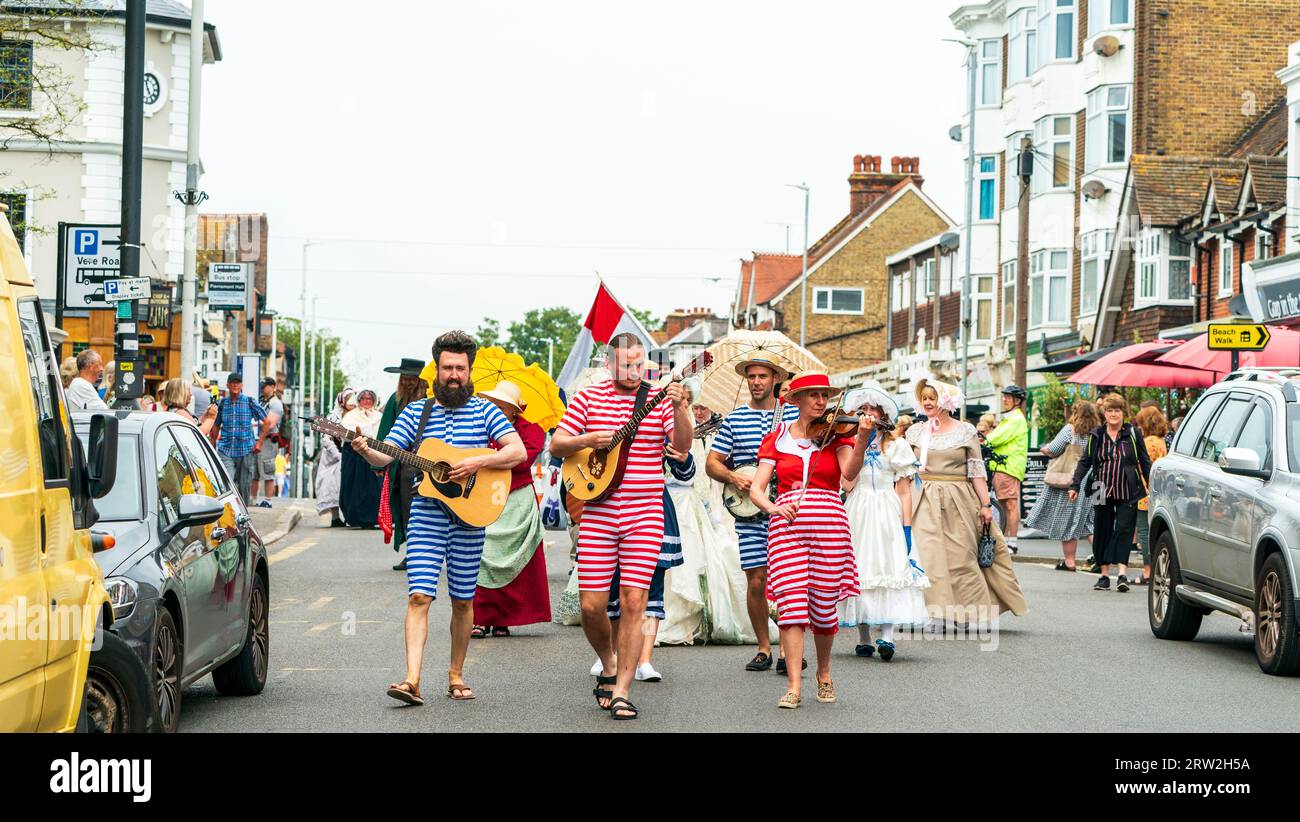 Parade von Menschen in viktorianischen Kostümen, angeführt von einem Quintett aus fünf Musikern, die in Strandkleidung gekleidet sind und durch die High Street in Broadstairs marschieren. Stockfoto