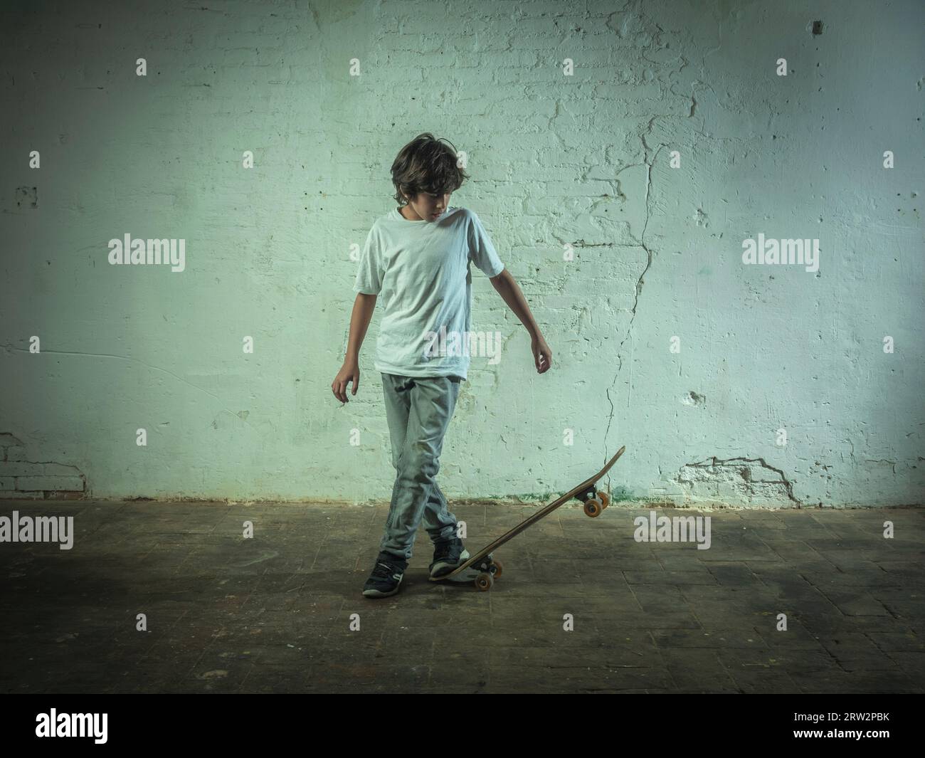 Junge, der Skateboarding vor einer alten weißen Ziegelmauer übt. Stockfoto