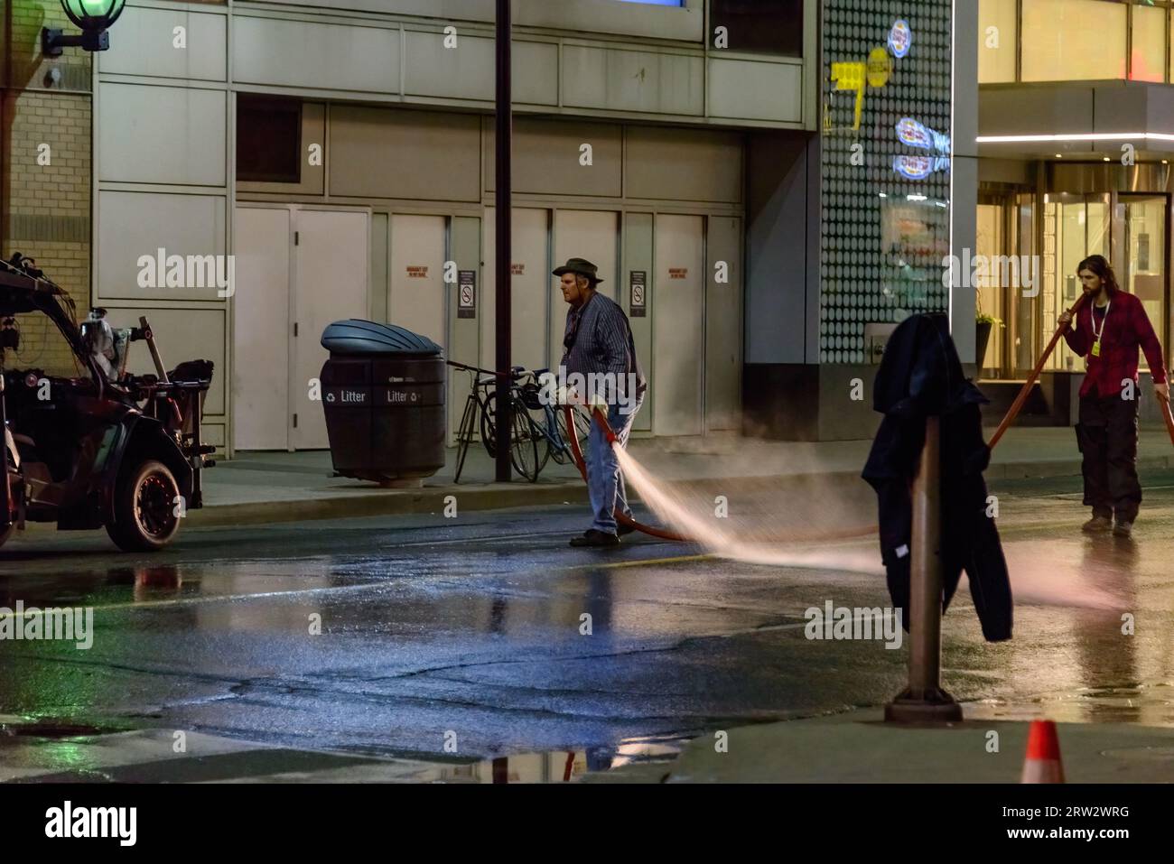 Zwei Filmcrew-Mitglieder benutzen einen großen Schlauch und verteilen Wasser auf dem Bürgersteig der Yonge Street. Stockfoto