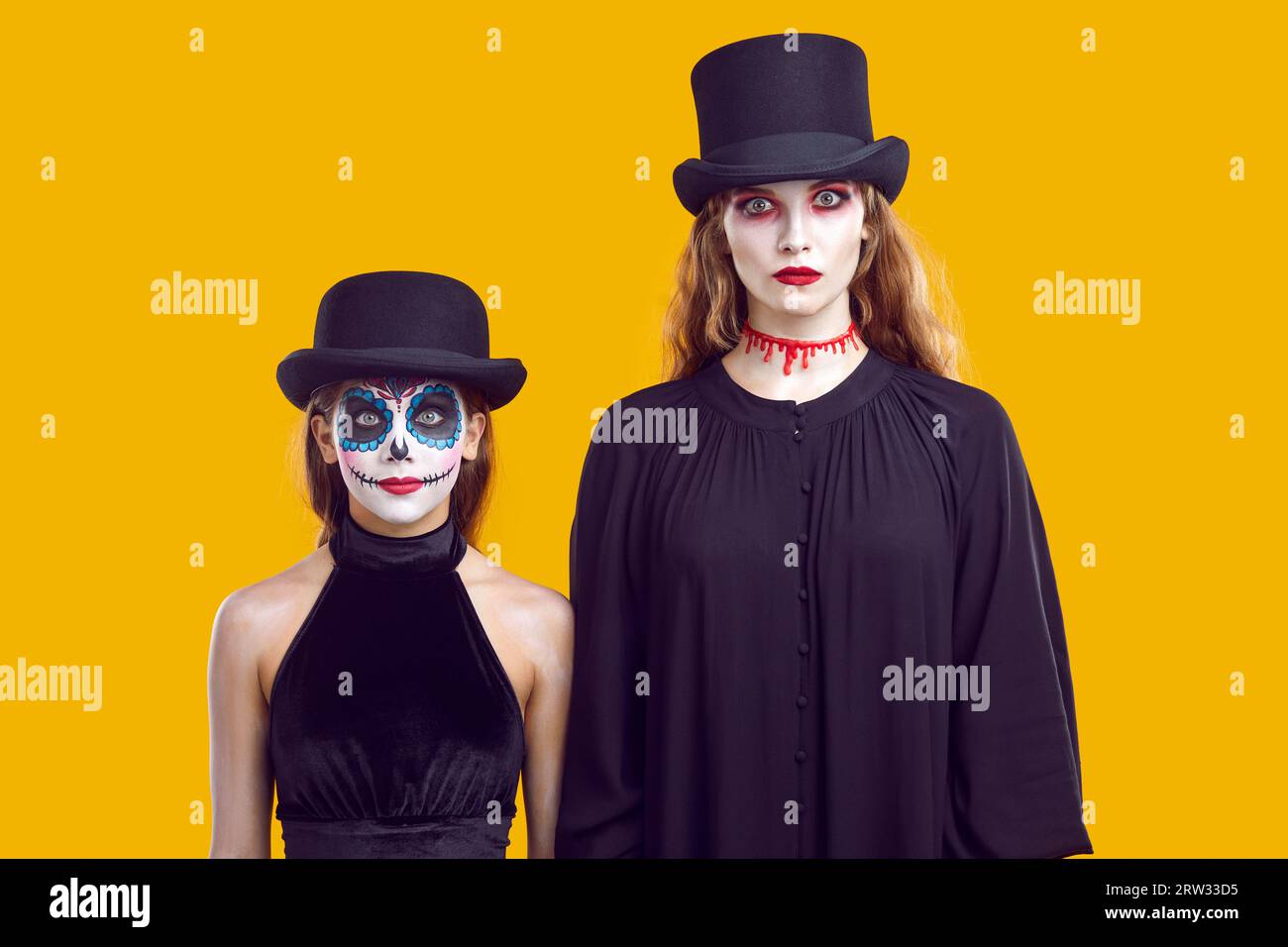 Ernsthafte Mutter und Tochter in Halloween-Outfits, die dich anschauen und auf Trick oder Leckerei warten. Stockfoto