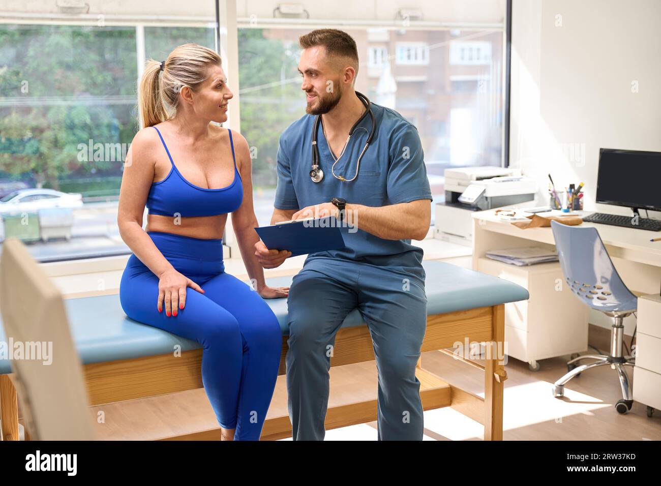 Männlicher Rehabilitologiespezialist spricht mit Frau und zeigt ihren Heilfortschritt Stockfoto