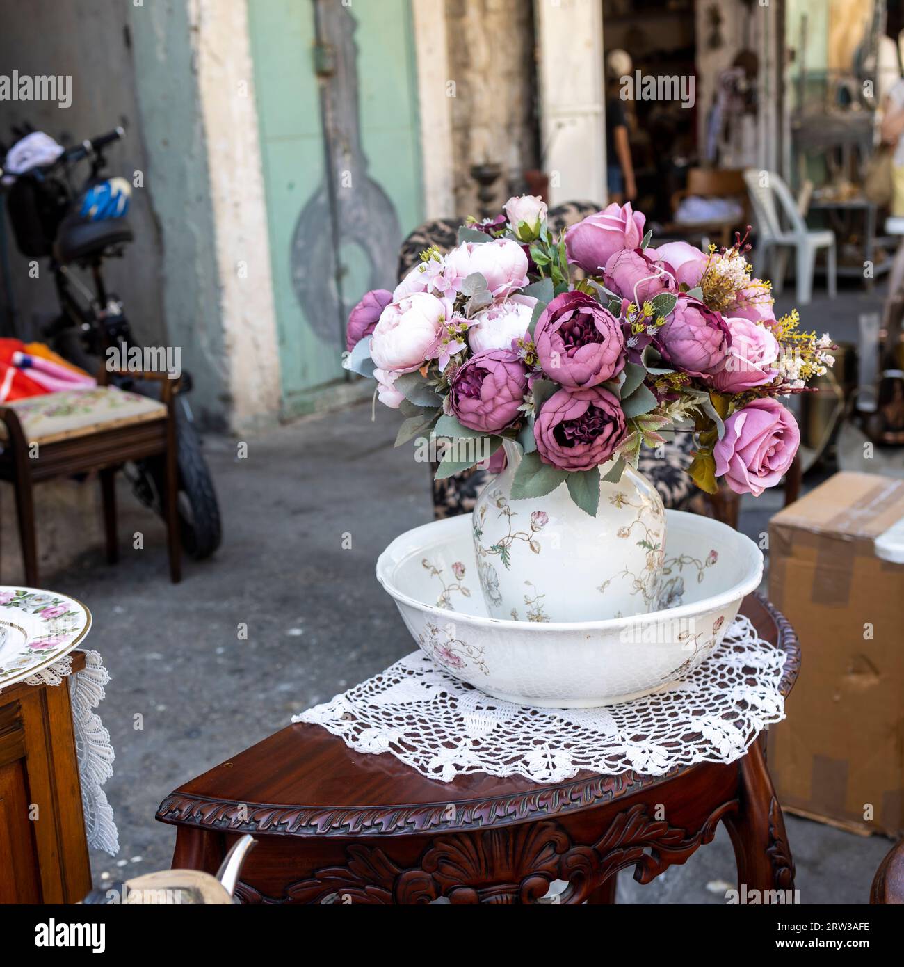 Ein Blumenstrauß aus künstlichen Rosen, Hortensien, Pfingstrosen, Gänseblümchen in einem weißen Keramikkrug auf einem Flohmarkt auf einem Tisch. Stockfoto