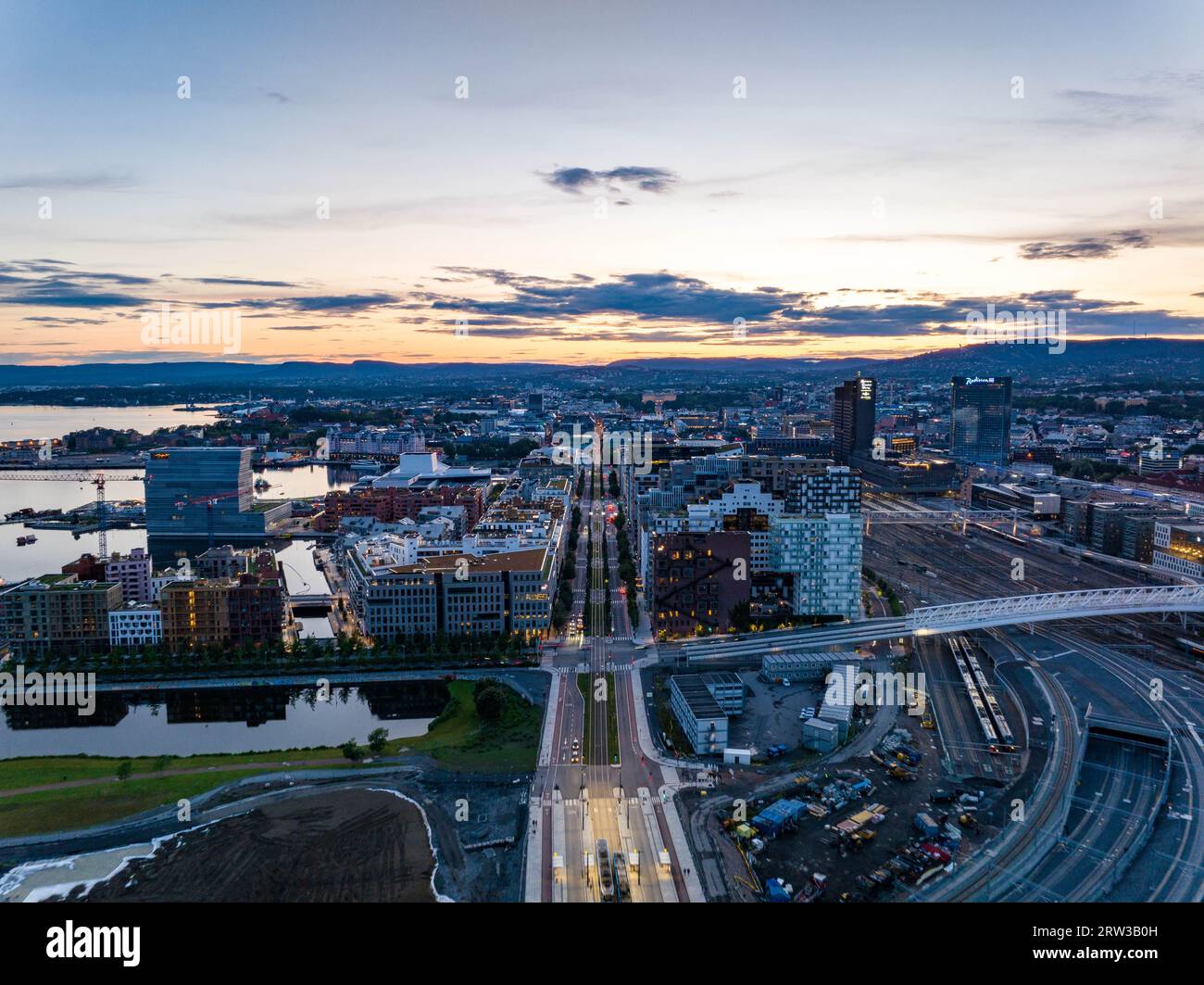 Blick aus der Vogelperspektive auf den modernen Stadtbezirk am Hauptbahnhof vor dem farbenfrohen Sonnenuntergang. Ruhige Wasseroberfläche, die den Himmel reflektiert. Oslo, Norwegen Stockfoto