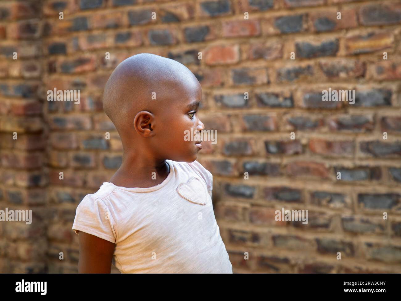 Junger afrikanischer dorfbewohner mit Glatzkopf, der draußen vor einer Ziegelmauer steht Stockfoto