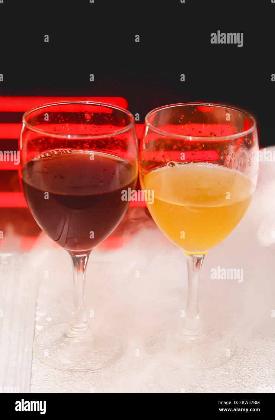 2 zwei Gläser mit alkoholischen Getränken in weißem Shisha-Rauch oder flüssigem Eisrauch auf abstraktem rotem schwarzem Hintergrund. Stockfoto