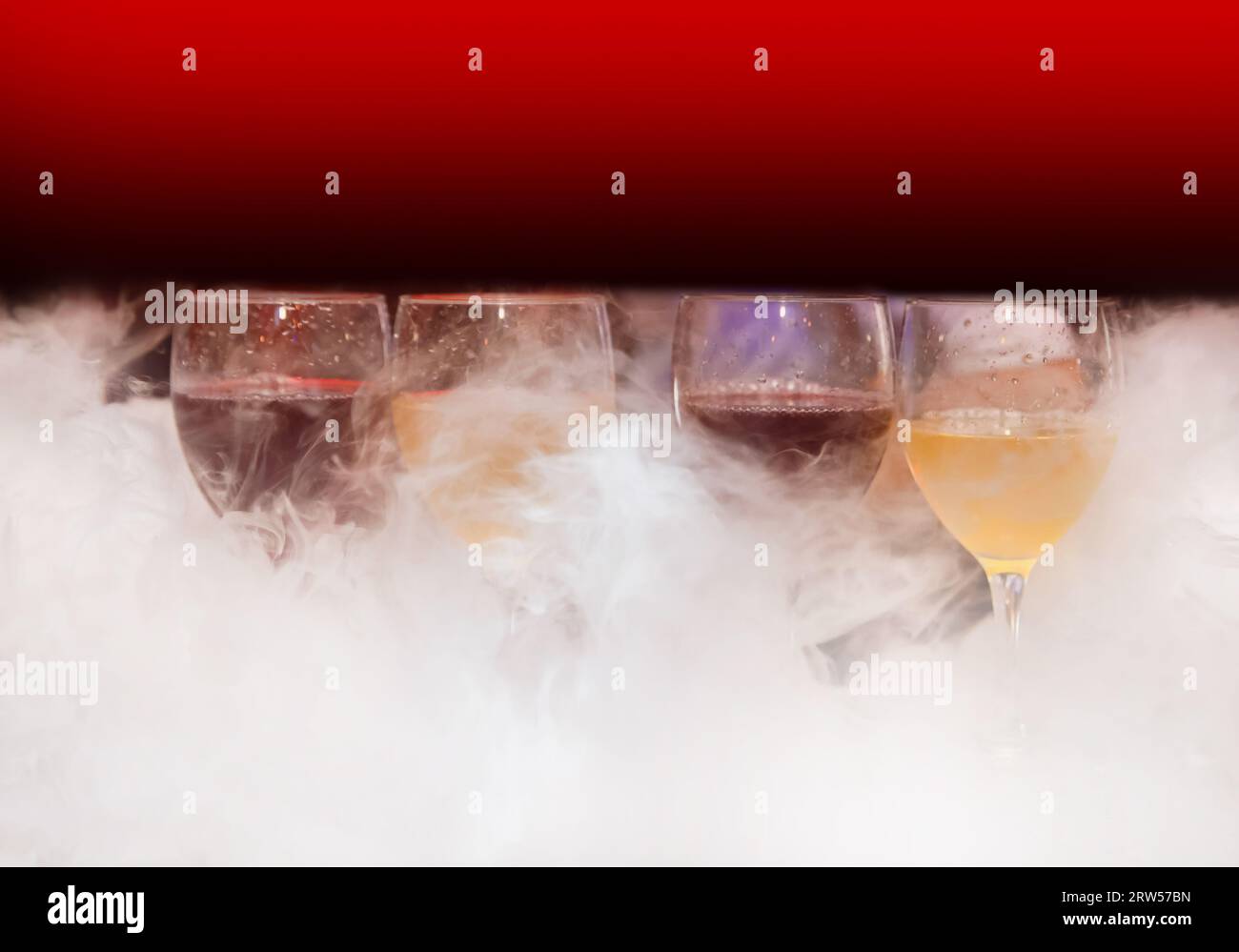 Vier Gläser mit alkoholischen Getränken in weißem Shisha-Rauch oder flüssigem Eisrauch auf abstraktem Hintergrund. Stockfoto