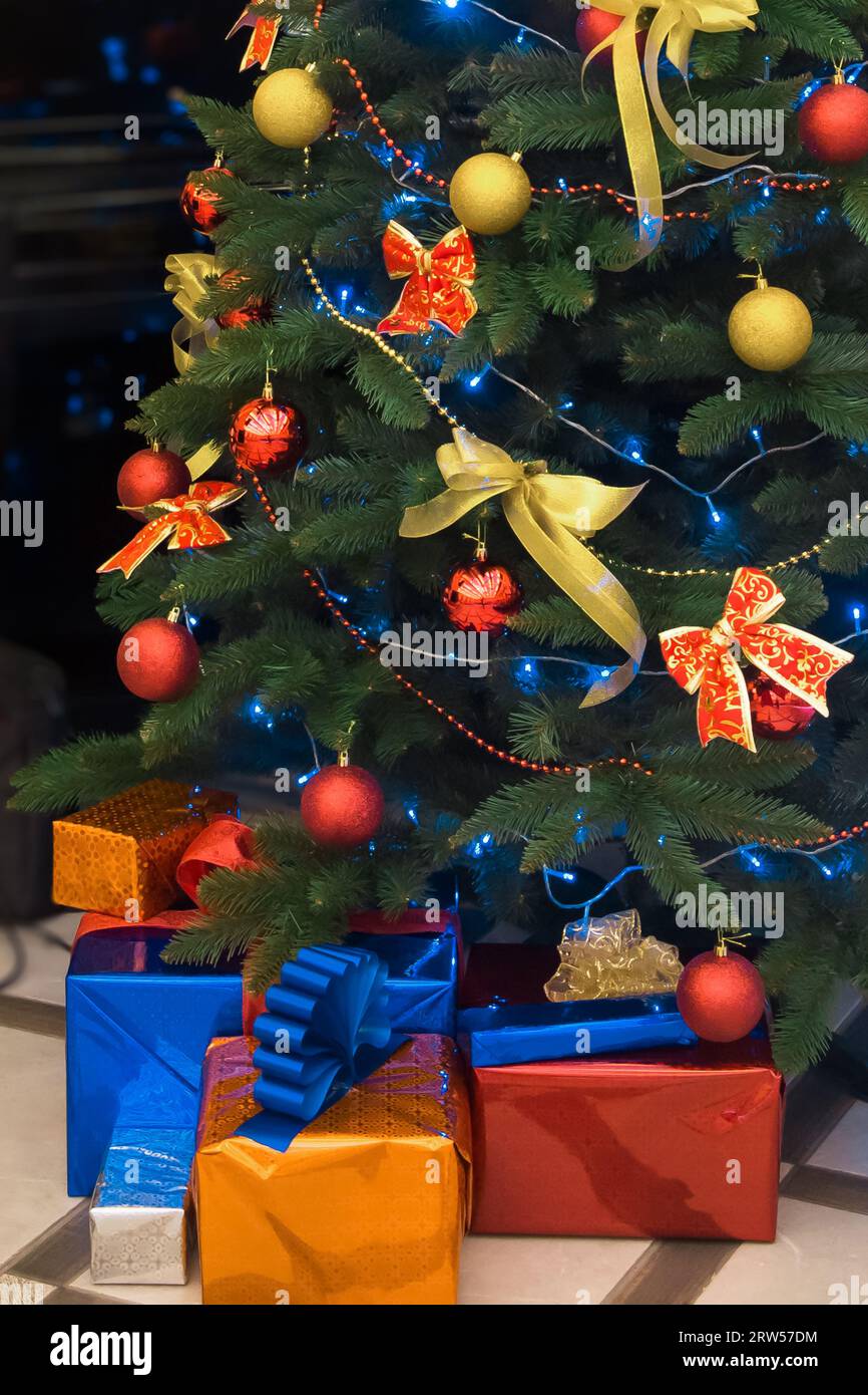 Der grüne Weihnachtsbaum, der mit Spielzeug, Ballons und Bändern mit Geschenken in Kisten verziert ist, ist die Atmosphäre darunter. Stockfoto