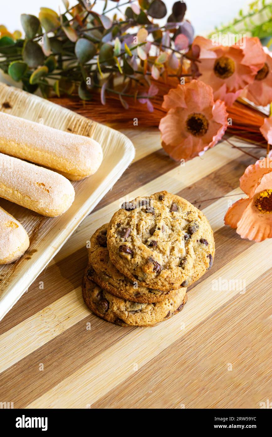 Hausgemachte Plätzchen mit Schokoladenstückchen auf Holztisch mit einigen Blumen und Blättern als Dekoration. Stockfoto