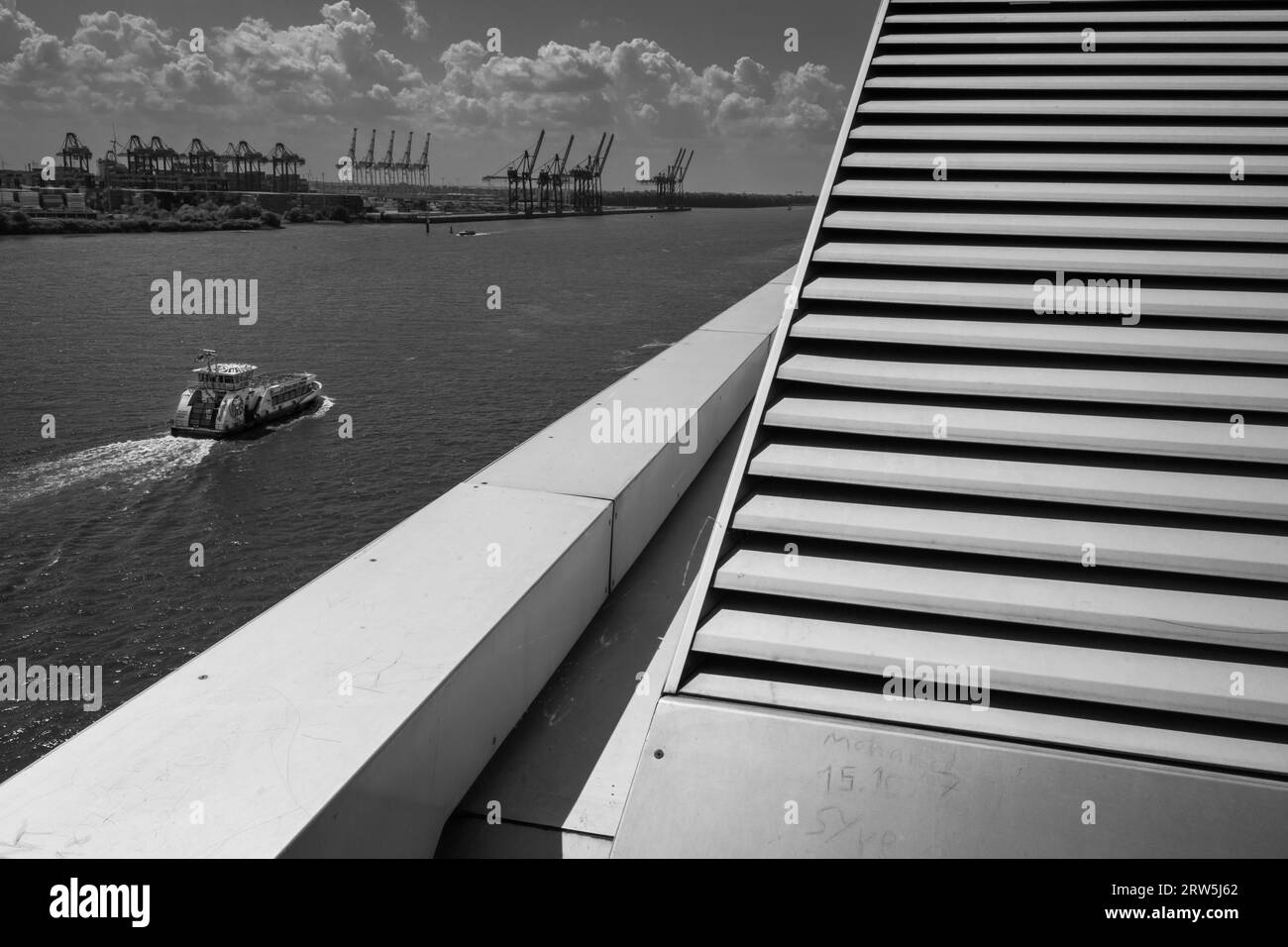 Hamburg, Deutschland - 17. Juni 2023: Elblandschaft mit Hafenkranen, Hafengebäude und Fähre in Schwarz-weiß Stockfoto