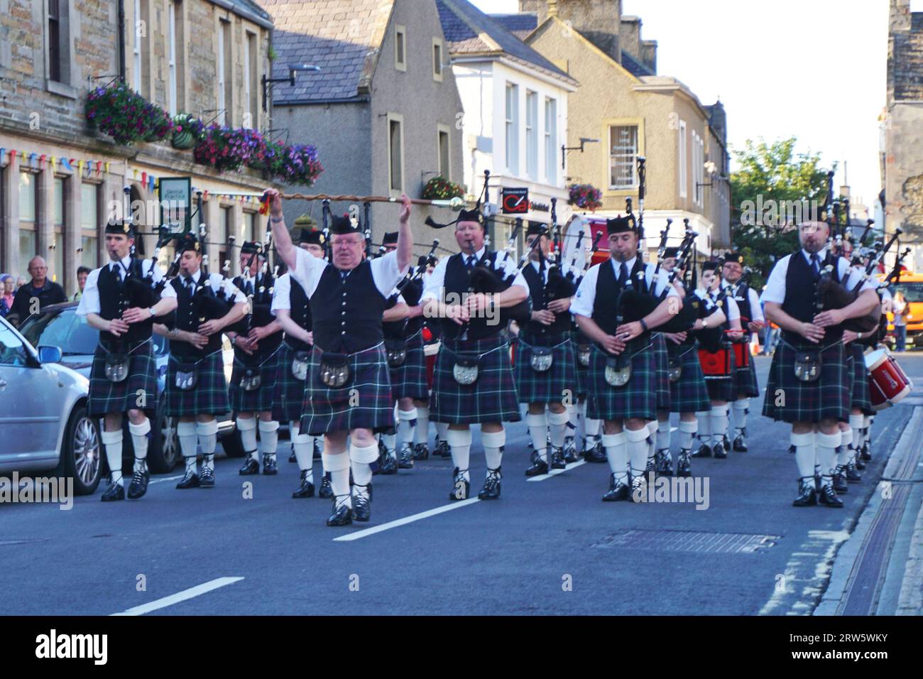 Die Kirkwall City Pipe Band kommt zum Stehen, als der Schlagzeuger vor der Formation in der Innenstadt von Kirkwall, Orkney Island, seine Streitkraft in die Luft hebt Stockfoto