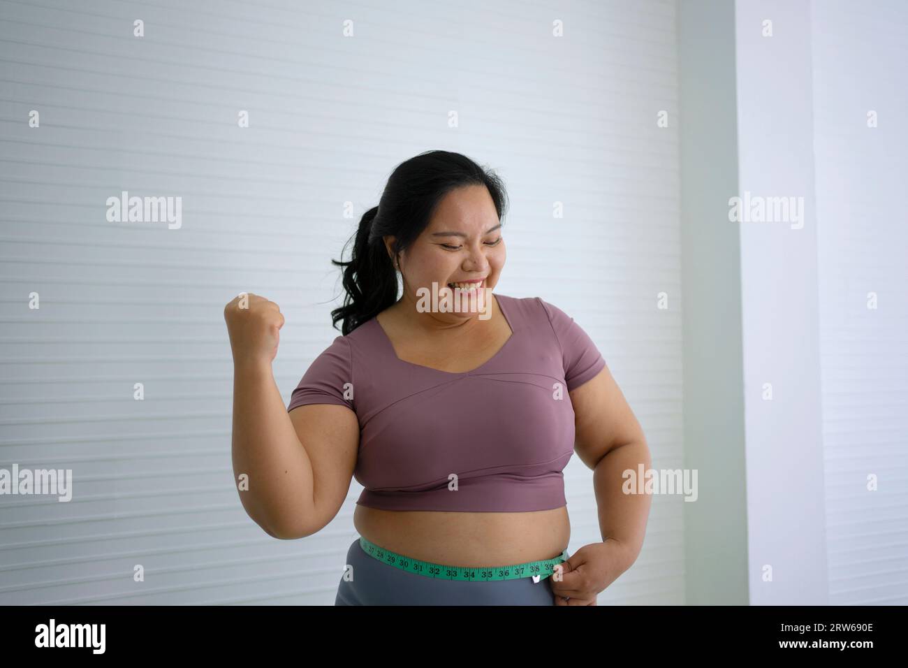 Plus Size Frau misst ihre Taille nach dem Training. Gesundheits- und Lifestyle-Konzept. Stockfoto