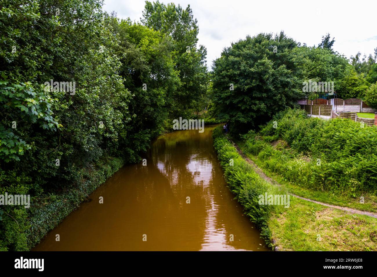 Schattiger Teil des Trent und Mersey Canal, Kidsgrove, Newcastle-under-Lyme. Das Wasser ist orange, denn wenn sich Lehm im Harecastle-Tunnel ablagert, la Stockfoto