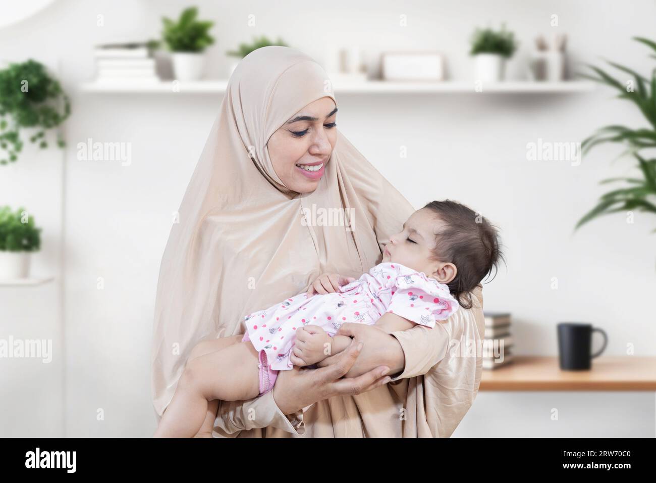 Porträt einer lächelnden jungen muslimischen Mutter, die Hijab trägt und ihr süßes kleines Baby hält. Stockfoto