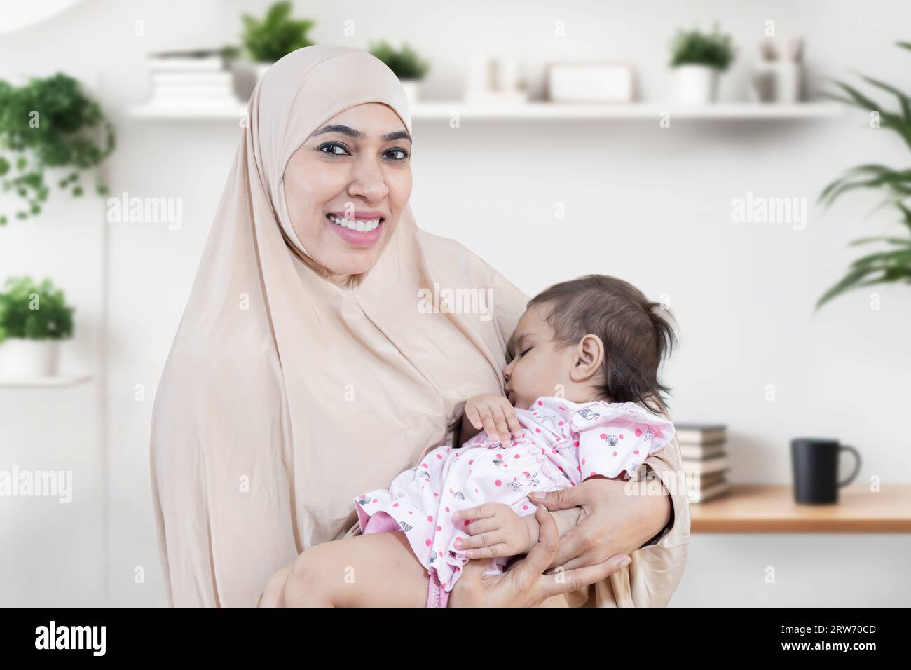 Porträt einer lächelnden jungen muslimischen Mutter, die Hijab trägt und ihr süßes kleines Baby hält. Stockfoto