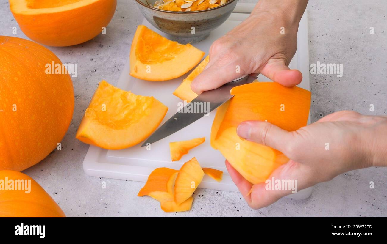 Frau Hände schälen frischen rohen orangen Kürbis, Nahaufnahme auf grauem Stein Hintergrund Stockfoto