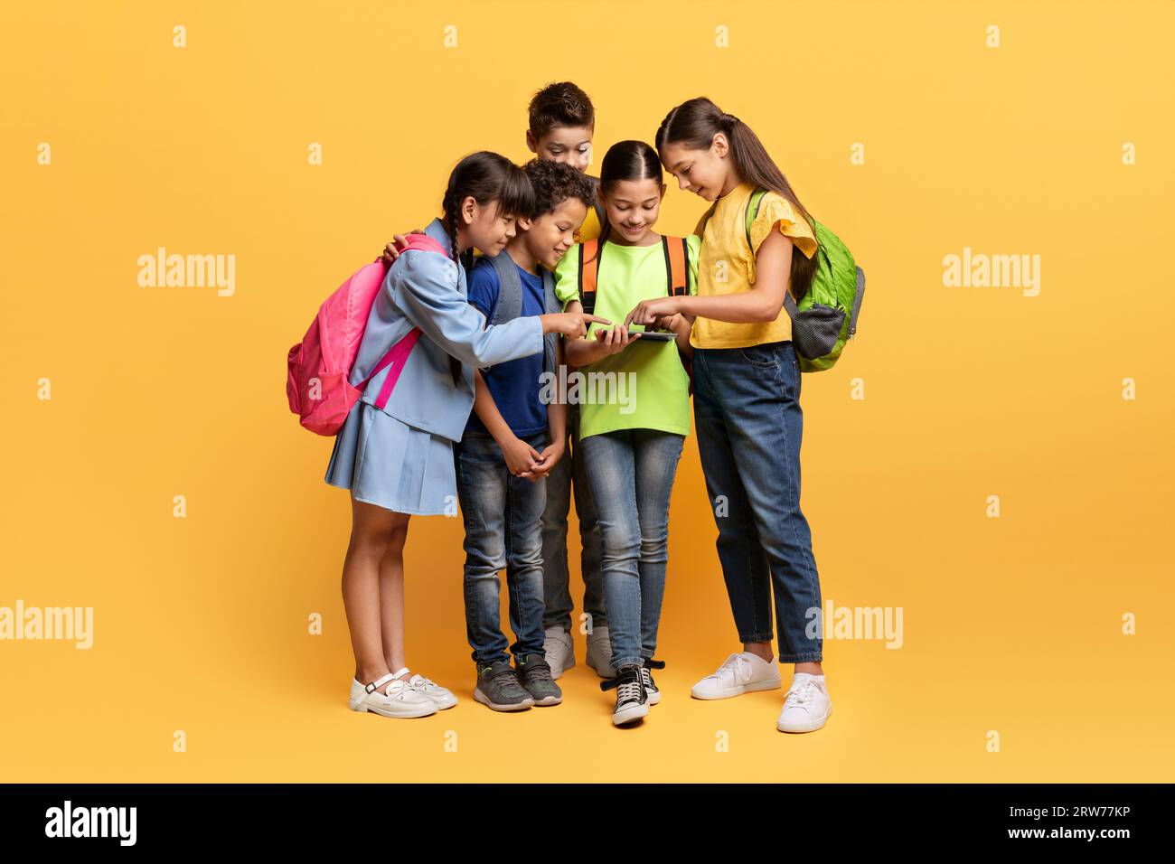 Niedliche multiethnische Schulkinder, die ein digitales Tablet auf gelb sehen Stockfoto