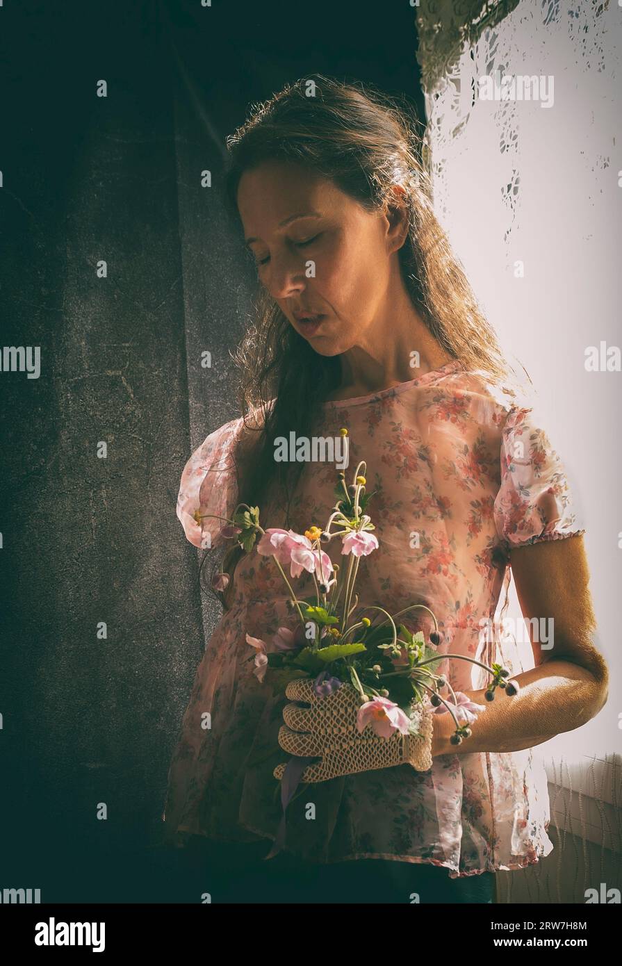 Frau mit Blumenstrauß in der Nähe von Fenster V Stockfoto