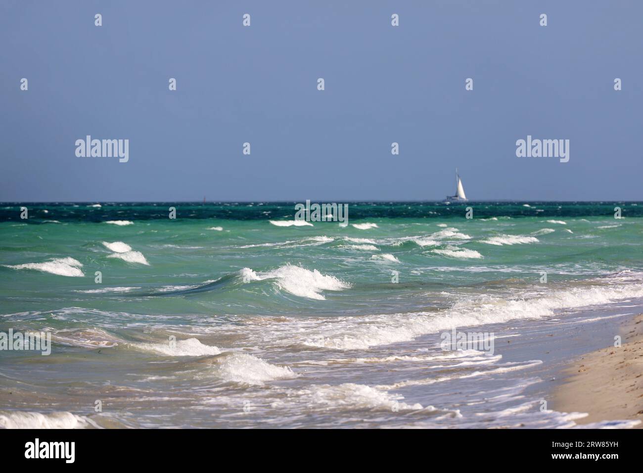 Leerer Strand, Blick auf die Wellen und Segelboot in der Entfernung. Meeresküste, Hintergrund für Urlaub Stockfoto