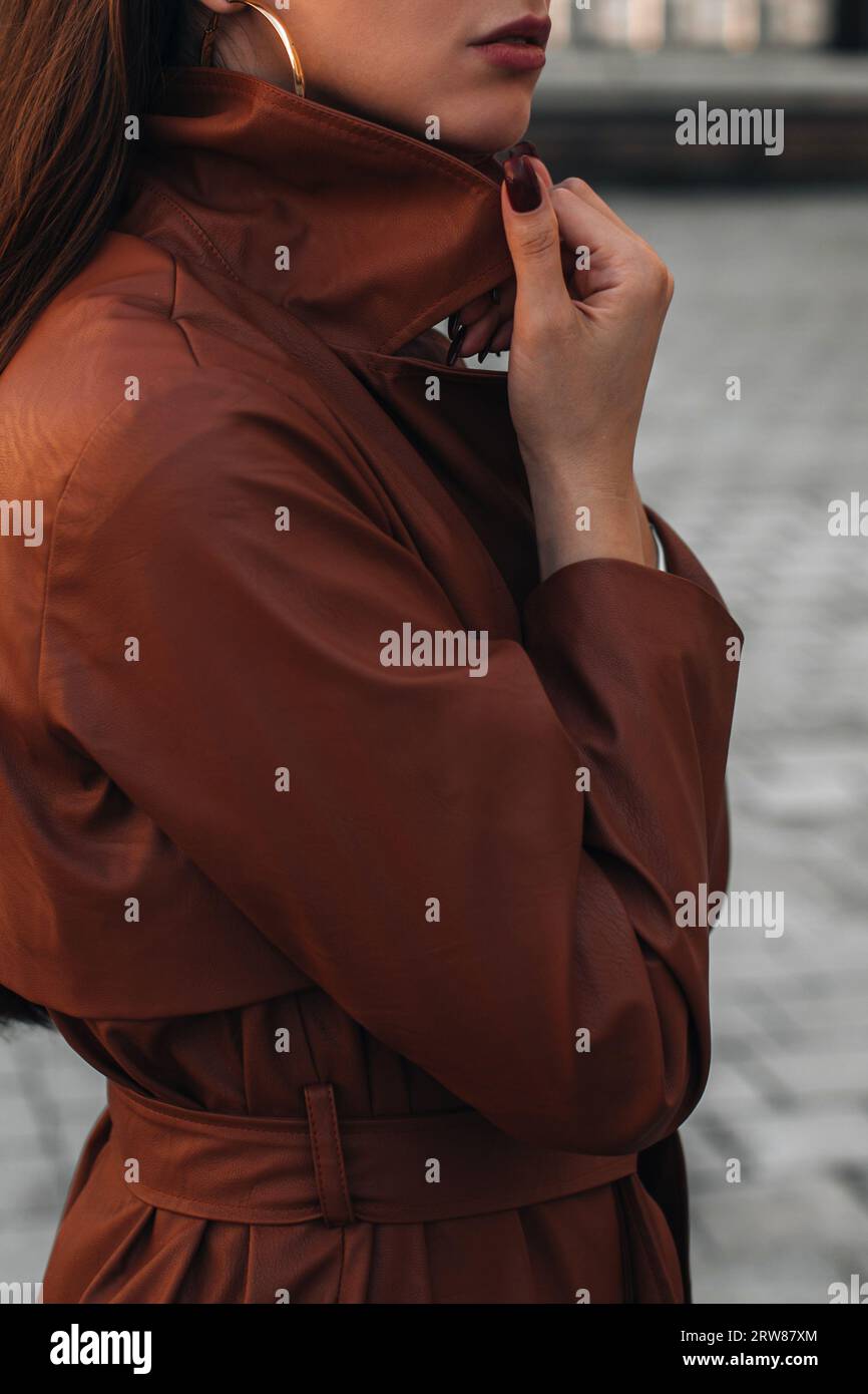 Modische Details eines langen braunen Ledertrenchjacken im Herbst. Lässige Kleidung im Streetstyle. Eine Frau, die allein in der Stadt läuft. Stockfoto