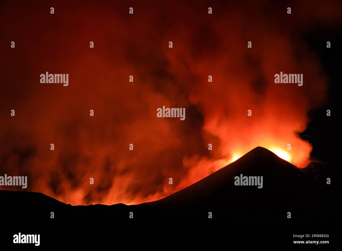 Ätna in einem nächtlichen Lavaausbruch mit hinterleuchteten Silhouettenkrater und großen Rauchemissionen in einem Panoramablick auf den Vulkan sizilien Stockfoto