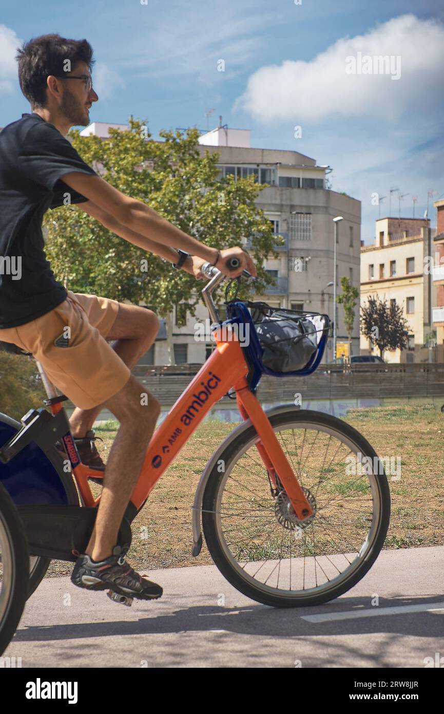 Viladecans, Spanien - 18. September 2023: Junger kaukasischer Mann in Shorts und T-Shirt lächelnd mit Brille auf dem Radweg eines Parks und eines Elektrofahrzeugs Stockfoto