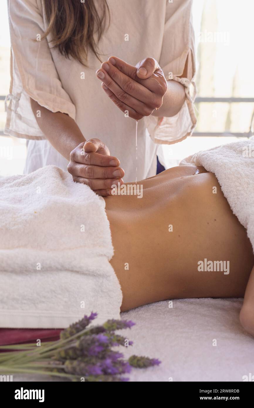 Nahaufnahme einer Therapeutin, die vor der Therapie Massageöl auf die Hände aufträgt, über die Dame, die auf dem Massagetisch liegt. Stockfoto