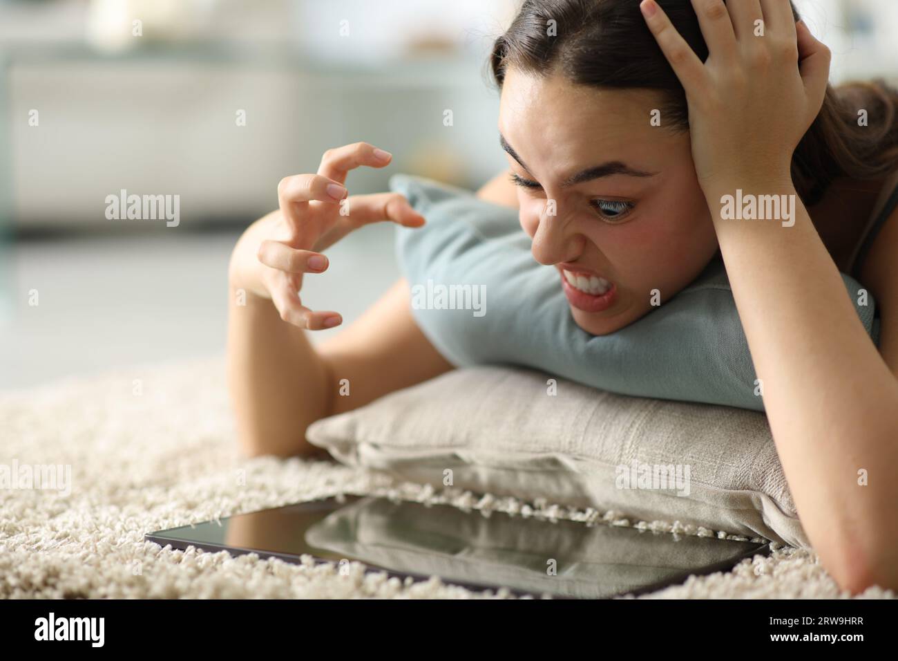 Verärgerte Frau, die zu Hause auf dem Boden liegt und den Inhalt des Tablets überprüft Stockfoto