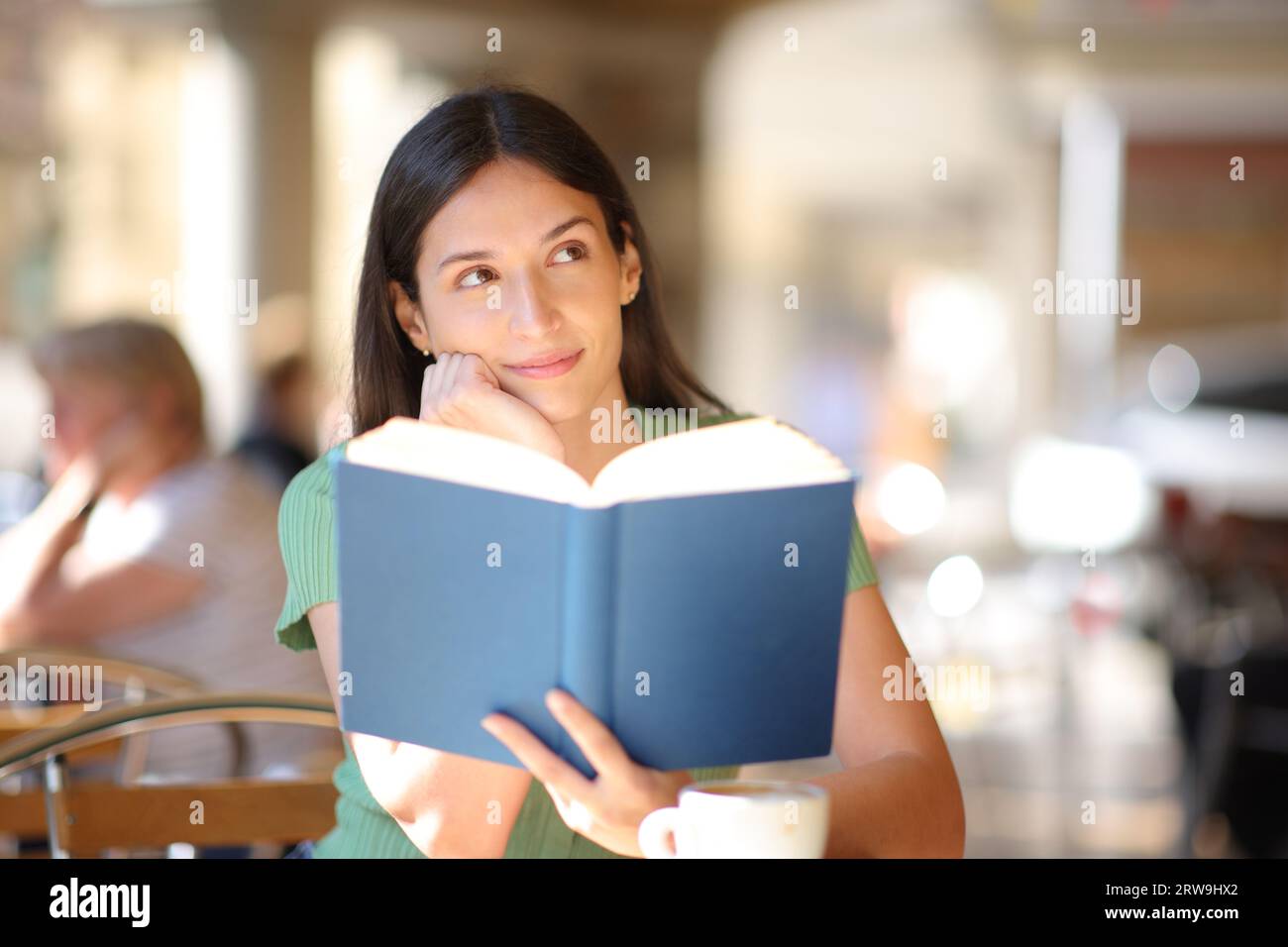 Blick von vorne auf einen glücklichen Buchleser, der träumte und auf die Seite in einer Bar-Terrasse blickte Stockfoto