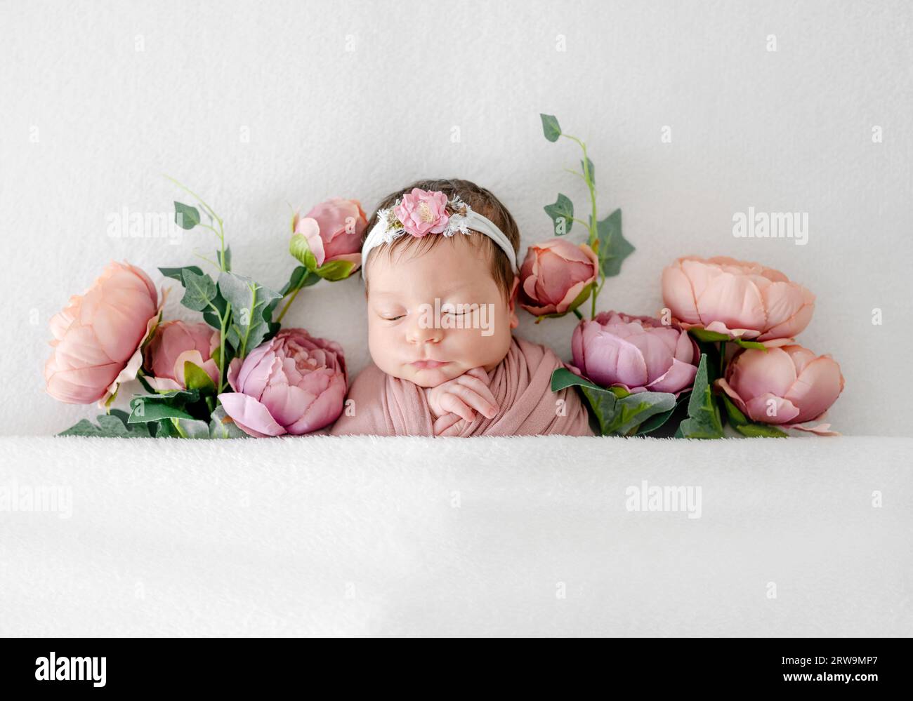 Entzückendes Neugeborenes, das in Pfingstrosenblüten schläft. Niedliches Kind, das in rosa Pflanzen schläft und einen Kranz trägt Stockfoto