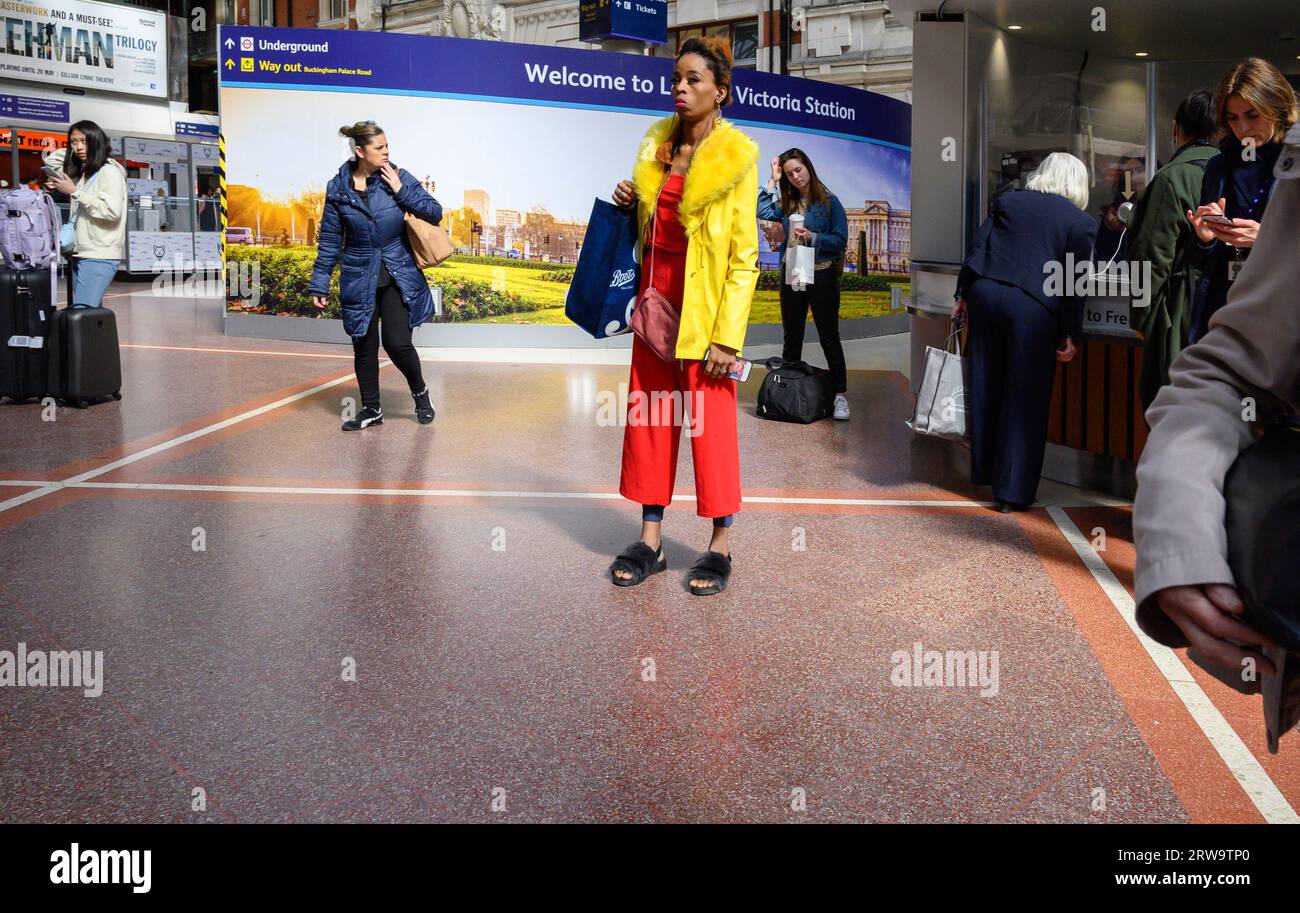 London, Großbritannien. Frau in hellen Farben gekleidet in der Halle der Victoria Station Stockfoto