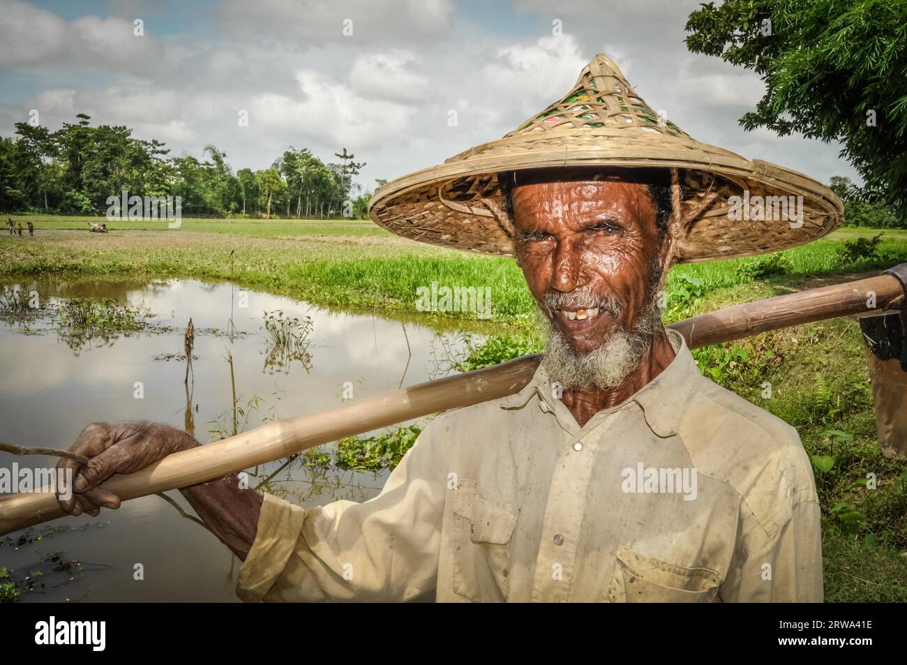 Srimongal, Bangladesch, um Juli 2012: Ein alter Mann mit Falten im Gesicht und grauem Bart hält in Srimongal einen Holzstock auf der Schulter Stockfoto