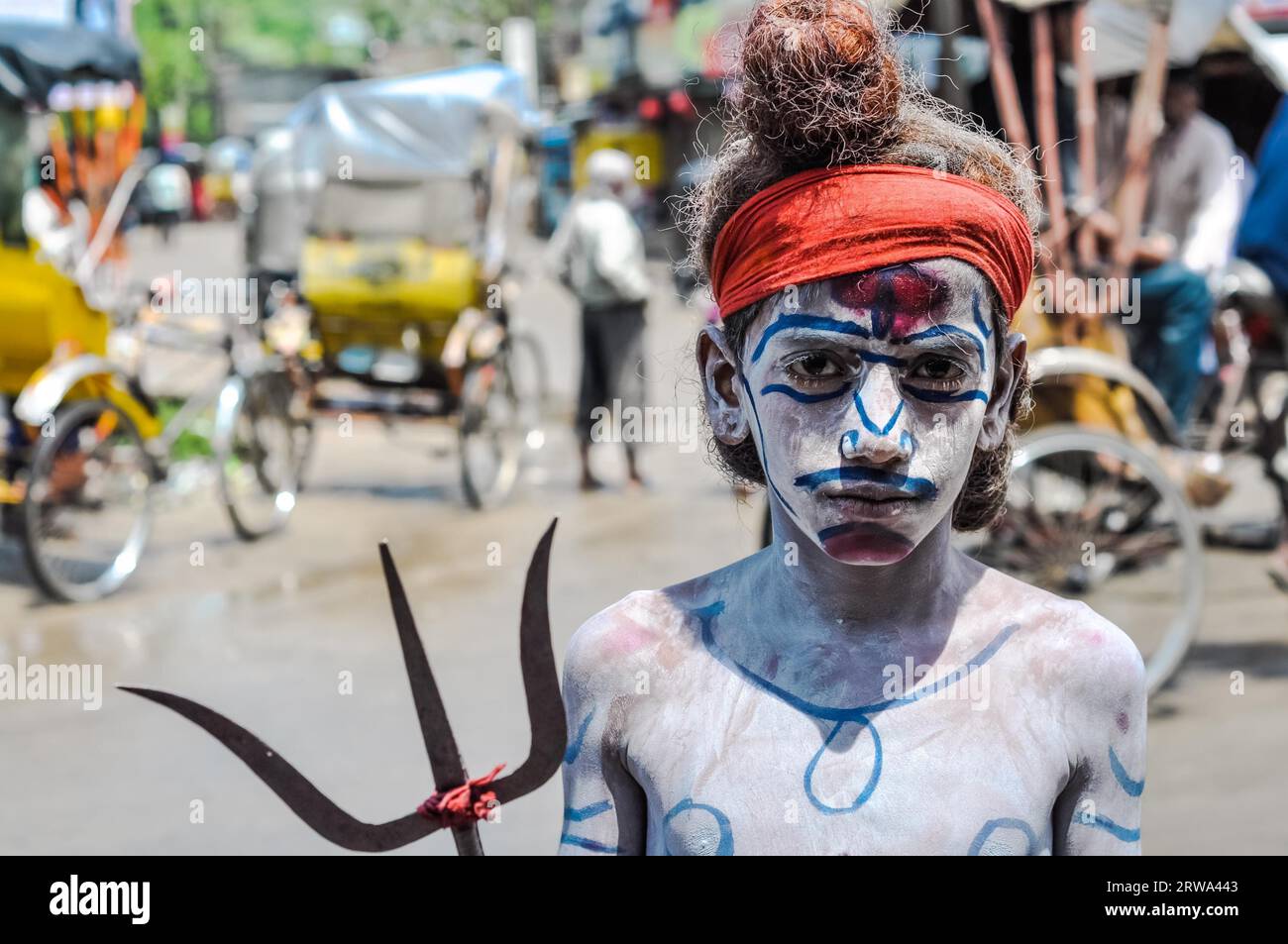 Silchar, Assam, um April 2012: Junge mit orangem Stirnband und mit weißem Puder und Farben bedecktem Körper hält Pitchfork in Silchar, Assam. Stockfoto