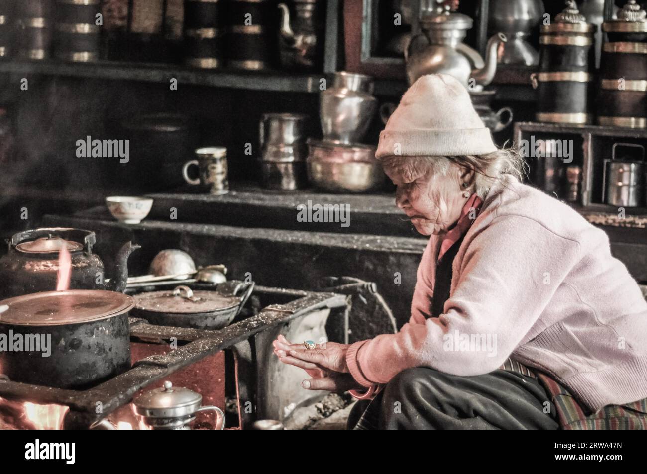 Kanchenjunga Trek, Nepal, ca. Mai 2012: Alte Frau mit weißer Kappe kniet in der Nähe des Ofens und schaut auf ihren Ring in Kanchenjunga Trek, Nepal. Stockfoto