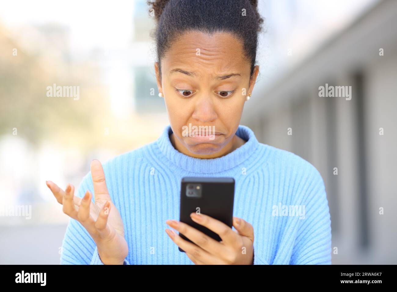 Porträt einer verblüfften schwarzen Frau, die ihr Handy auf der Straße überprüft Stockfoto