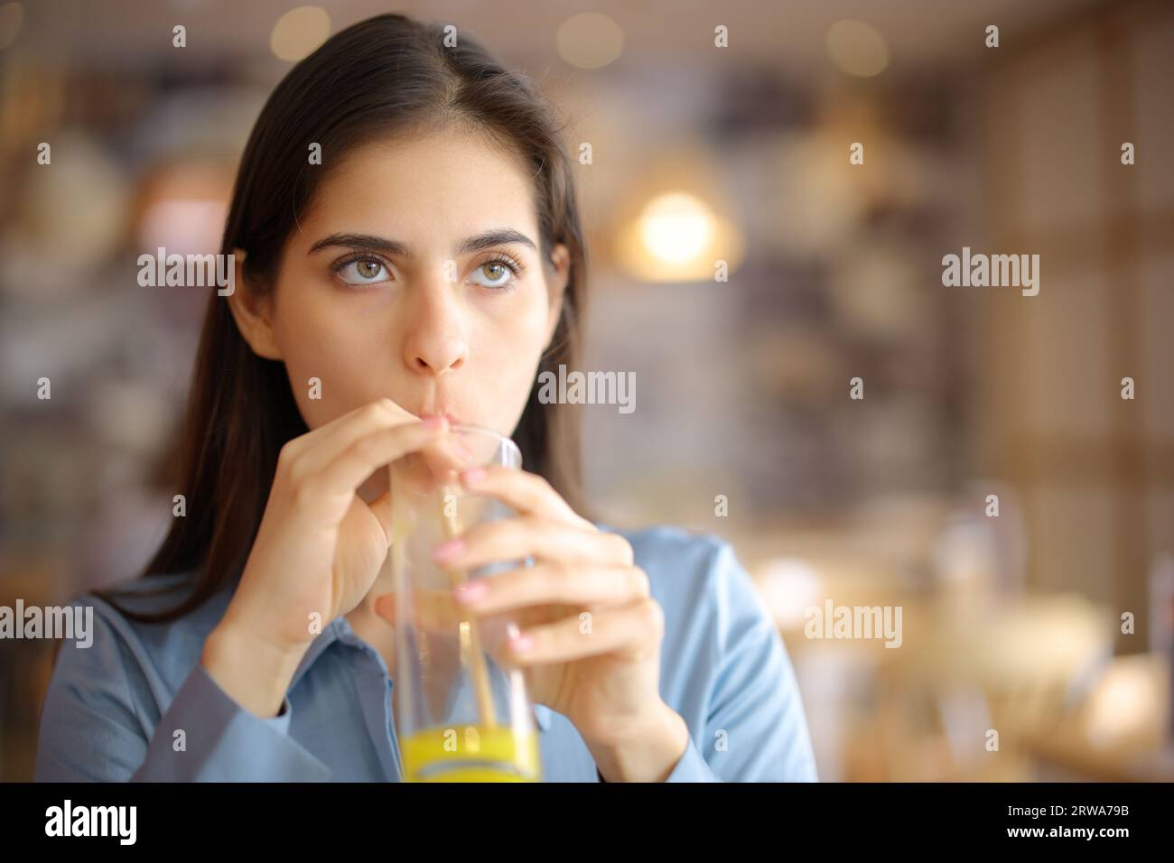 Vorderansicht einer abgelenkten Frau, die in einem Restaurant Orangensaft mit Strohhalm trinkt Stockfoto