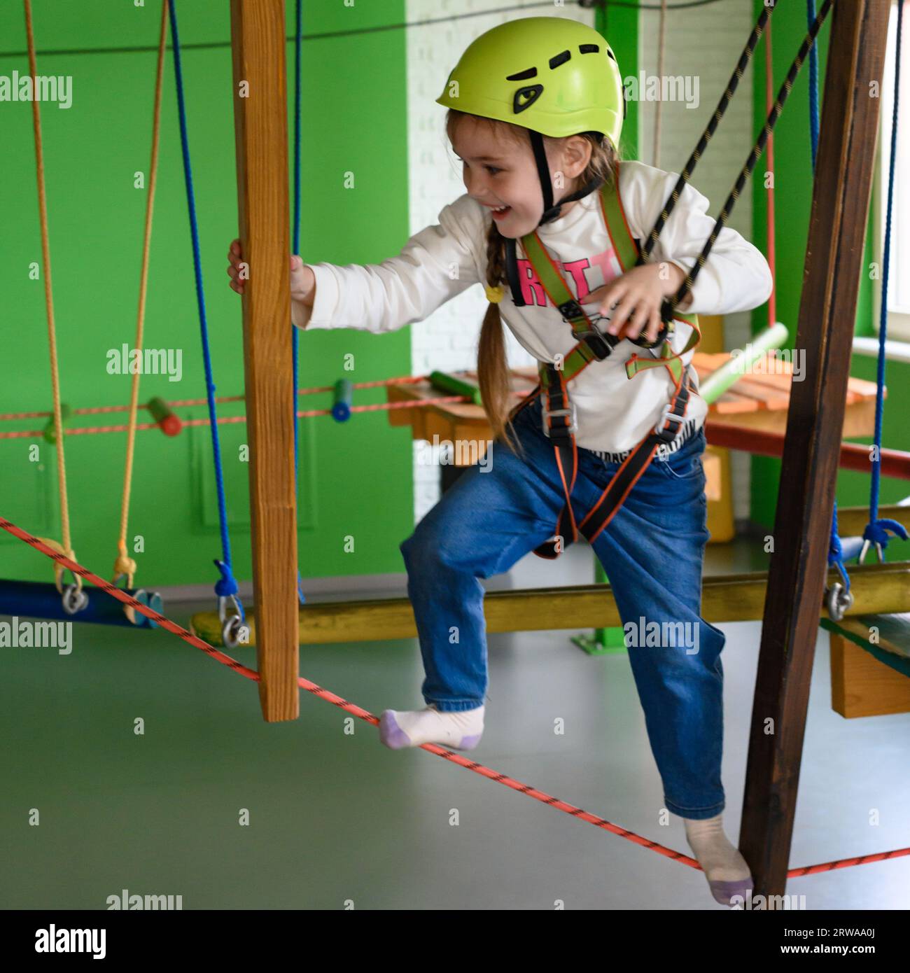 Glückliches Mädchen passiert die Seilbahn, aktive Erholung im Spielzimmer, Seilbahn für die körperliche Entwicklung des Kindes. Stockfoto