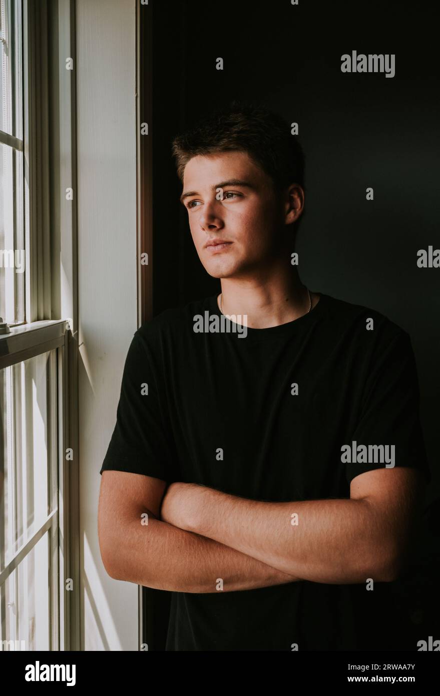Porträt eines hübschen Teenagers, der aus dem Fenster des dunklen Zimmers schaut. Stockfoto