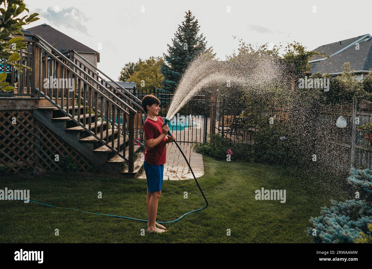 Junge, die den Garten im Garten mit Schlauch am Sommertag bewässern. Stockfoto