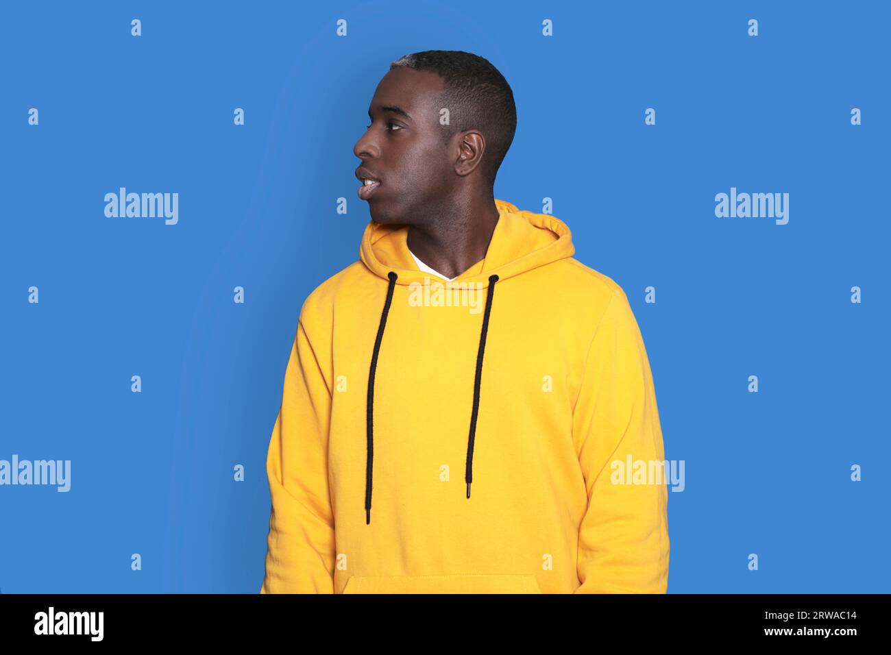 Ein Porträt eines fröhlichen jungen afroamerikanischen Mannes, der einen gelben Hoodie trägt und isoliert auf blauem Hintergrund posiert. Ein unbeschwerter junger Millennials-Mann Stockfoto