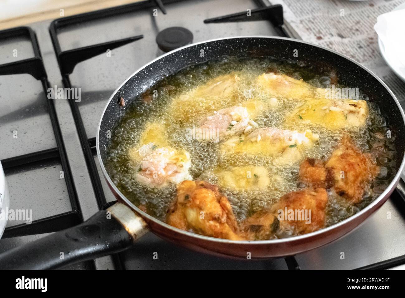 Hähnchenflügel in heissem Pflanzenpalmöl in der Pfanne anbraten Stockfoto