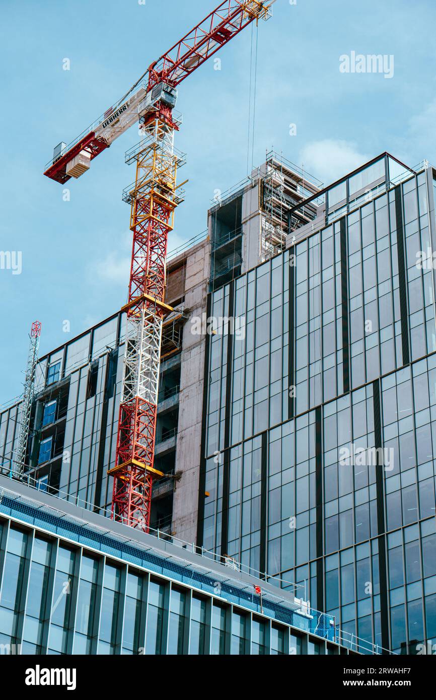 Glas- und Stahlgebäude im Bau, mit blauem Himmel und einem rot-weißen Kran davor. Stockfoto