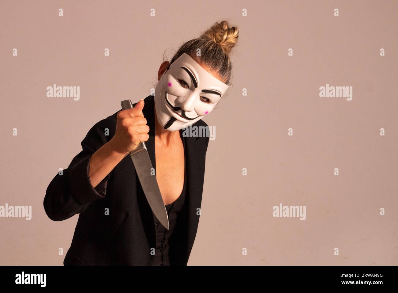Frau mit einer anonymen Maske in einer schwarzen Anzugjacke, mit einem Messer in der Hand, vorbereitet für die Halloween-Party Stockfoto
